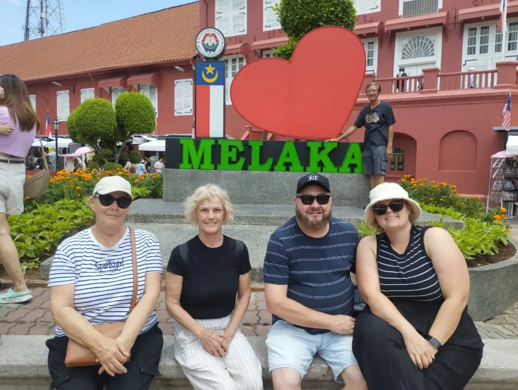 Previous Malacca tour guests seated at the I Love Melaka sign in Dutch Square